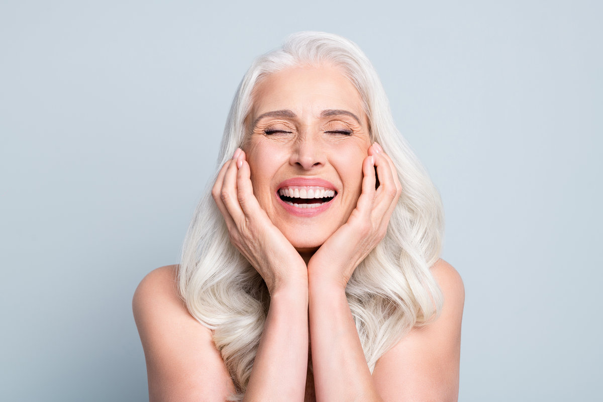Smiling older woman laughing with her hands on her cheeks